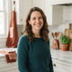 A friendly woman smiling in a clean kitchen with warm terracotta and white decor.
